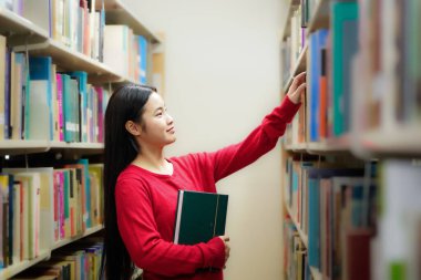 Üniversitede kütüphanede kitaplıkta kitap arayan öğrencilerin yan görünümü.