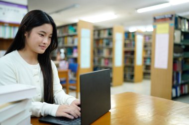 Genç üniversiteli kadın kütüphanede tek başına çalışırken bilgisayarında çalışıyor...