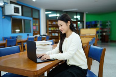 Genç üniversiteli kadın kütüphanede tek başına çalışırken bilgisayarında çalışıyor...