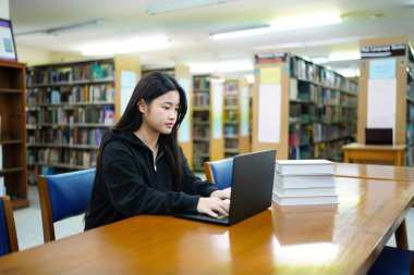 Genç üniversiteli kadın kütüphanede tek başına çalışırken bilgisayarında çalışıyor...