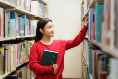 Üniversitede kütüphanede kitaplıkta kitap arayan öğrencilerin yan görünümü.