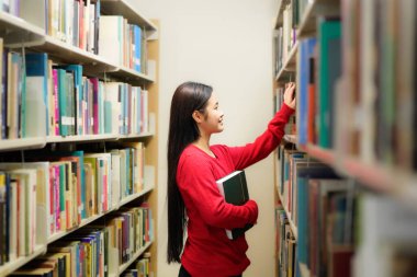 Üniversitede kütüphanede kitaplıkta kitap arayan öğrencilerin yan görünümü.