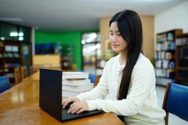 Genç üniversiteli kadın kütüphanede tek başına çalışırken bilgisayarında çalışıyor...