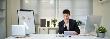 Asyalı adam çalıştığı yerde bilgisayar ve tablet kullanıyor. İşine odaklan...