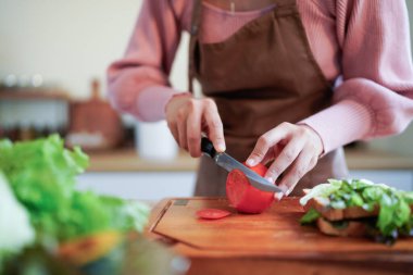 Parlak bir mutfakta ahşap bir kesme tahtasıyla taze domatesleri doğrayan birinin ellerine yakından bakın..