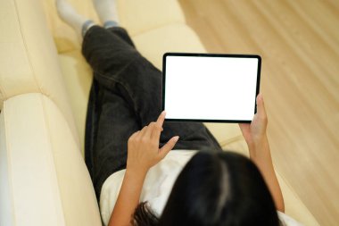 Evdeki kanepede yatarken elinde boş masaüstü beyaz ekran tableti olan bir kadının görüntüsü..