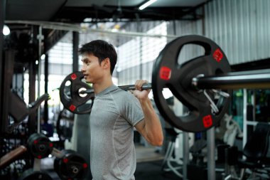 Bacaklarını ve sırtını çalıştırmak için spor salonunda halter kullanarak çömelen gri elbiseli bir vücut geliştiricinin portresi. Güçlü fitness egzersizi.