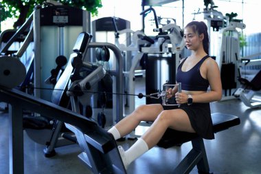 Spor salonunda ağırlık çeken, bisepslerini çalıştıran ve kas gücünü arttıran formda bir Asyalı kadın. Fitness Merkezi Sağlık Çalışmaları Konsepti.