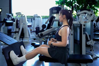 Spor salonunda ağırlık çeken, bisepslerini çalıştıran ve kas gücünü arttıran formda bir Asyalı kadın. Fitness Merkezi Sağlık Çalışmaları Konsepti.