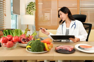 Üniformalı profesyonel beslenme uzmanı masaya farklı sağlıklı ürünler ve sağlıklı beslenmeyle ilgili çizimlerle notlar yazıyor..