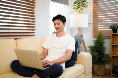 Genç bir adam oturma odasındaki kanepede dizüstü bilgisayar kullanıyor..