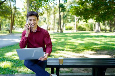 Profesyonel bir adam güneşli bir günde bilgisayarda çalışırken parkta telefonla konuşur..
