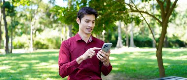 Genç Asyalı işadamı parkta akıllı telefon kullanıyor..
