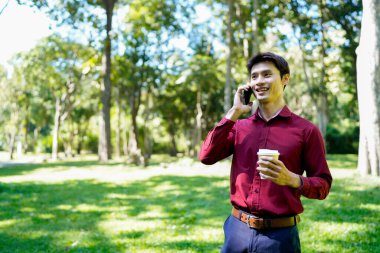 Paket kahveli genç Asyalı adam şehir parkında akıllı telefondan iletişim kuruyor..