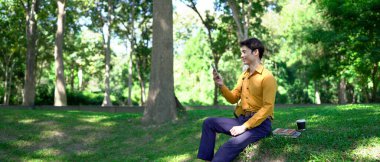 Genç Asyalı işadamı parkta akıllı telefon kullanıyor..