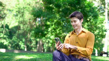 Genç Asyalı işadamı parkta akıllı telefon kullanıyor..