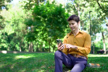 Genç Asyalı işadamı parkta akıllı telefon kullanıyor..