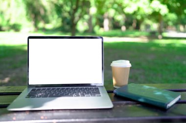 Laptop bilgisayarı, kahve fincanı yeşil bahçedeki ahşap masada...