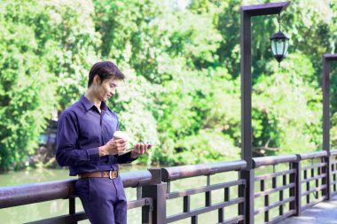 Elinde kahve fincanı olan bir adam ya da bahçede duran yeşil doğa arka planında duran tek kullanımlık kahve ve kitap. Mutlu insanları boş vakitlerinde kabul et ve kahve iç...