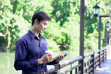 Elinde kahve fincanı olan bir adam ya da bahçede duran yeşil doğa arka planında duran tek kullanımlık kahve ve kitap. Mutlu insanları boş vakitlerinde kabul et ve kahve iç...