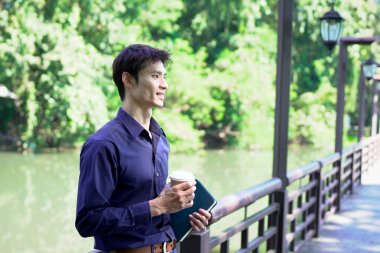 Elinde kahve fincanı olan bir adam ya da bahçede duran yeşil doğa arka planında duran tek kullanımlık kahve ve kitap. Mutlu insanları boş vakitlerinde kabul et ve kahve iç...