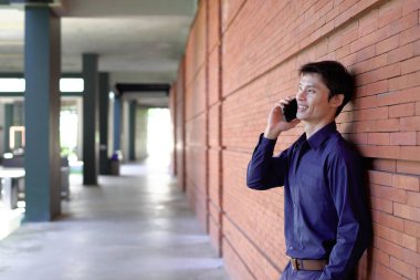 Gülümseyen iş adamı cep telefonuyla dışarıda oturuyor..