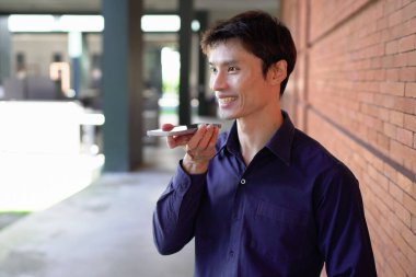 Gülümseyen iş adamı cep telefonuyla dışarıda oturuyor..