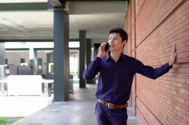 Gülümseyen iş adamı cep telefonuyla dışarıda oturuyor..