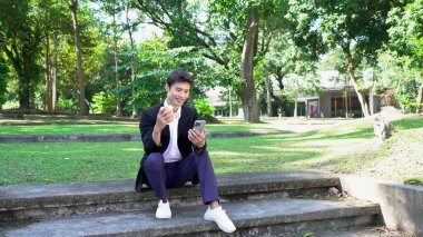 Gülümseyen işadamı akıllı telefon kullanıyor ve ofis binasının dışında kahve tutuyor..