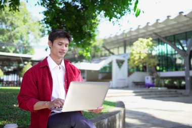 Erkek girişimci açık havada melez olarak oturuyor. Mutlu iş adamı girişimci ofis dışında dizüstü bilgisayar kullanarak başka tarafa bakıyor. Boşluğu kopyala..