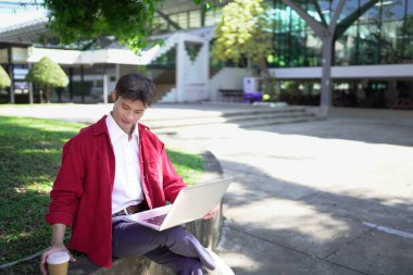 Erkek girişimci açık havada melez olarak oturuyor. Mutlu iş adamı girişimci ofis dışında dizüstü bilgisayar kullanarak başka tarafa bakıyor. Boşluğu kopyala..