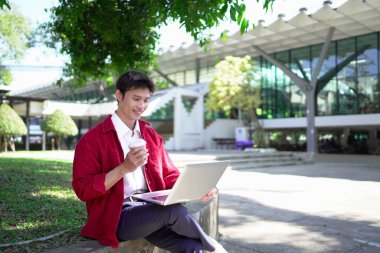 Uzaktan çalışan, kahve içen ve şehir parkında dizüstü bilgisayar kullanan bir adam..