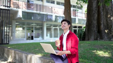 Uzaktan çalışan, kahve içen ve şehir parkında dizüstü bilgisayar kullanan bir adam..