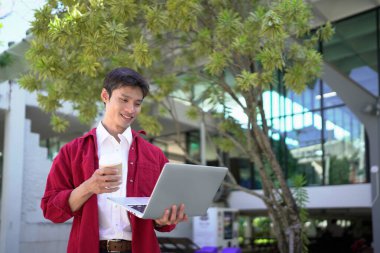 Uzaktan çalışan, kahve içen ve şehir parkında dizüstü bilgisayar kullanan bir adam..