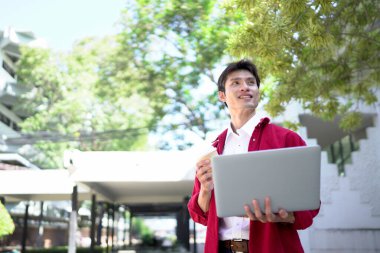 Uzaktan çalışan, kahve içen ve şehir parkında dizüstü bilgisayar kullanan bir adam..