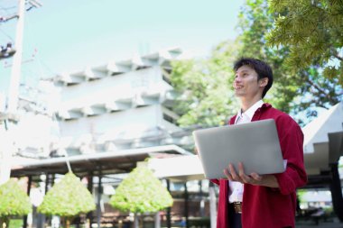 Uzaktan çalışan, kahve içen ve şehir parkında dizüstü bilgisayar kullanan bir adam..