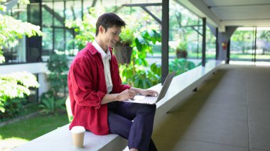 Erkek girişimci açık havada melez olarak oturuyor. Mutlu iş adamı girişimci ofis dışında dizüstü bilgisayar kullanarak başka tarafa bakıyor. Boşluğu kopyala..
