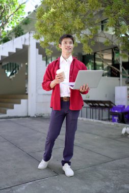 Uzaktan çalışan, kahve içen ve şehir parkında dizüstü bilgisayar kullanan bir adam..