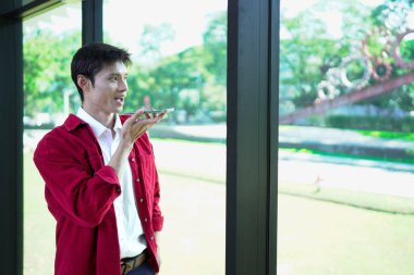 Genç bir adam sesli komut kullanıyor ya da akıllı telefonuyla yapay zeka asistanı ile iletişim kuruyor..