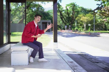 Akıllı telefonlu genç adam otobüs durağında toplu taşıma bekliyor..