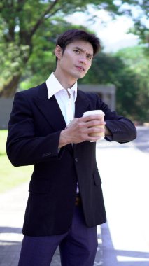 Siyah takım elbiseli bir işadamı kahve fincanı tutuyor, saatine bakıyor ve taksi bekliyor..