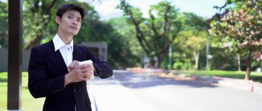 Siyah takım elbiseli bir işadamı kahve fincanı tutuyor, saatine bakıyor ve taksi bekliyor..