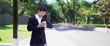 Siyah takım elbiseli bir işadamı kahve fincanı tutuyor, saatine bakıyor ve taksi bekliyor..