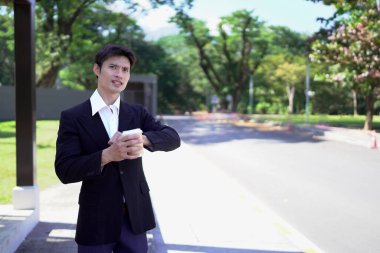 Siyah takım elbiseli bir işadamı kahve fincanı tutuyor, saatine bakıyor ve taksi bekliyor..