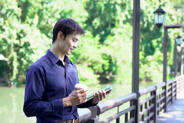 Elinde kahve fincanı olan bir adam ya da bahçede duran yeşil doğa arka planında duran tek kullanımlık kahve ve kitap. Mutlu insanları boş vakitlerinde kabul et ve kahve iç...