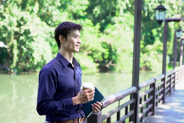 Elinde kahve fincanı olan bir adam ya da bahçede duran yeşil doğa arka planında duran tek kullanımlık kahve ve kitap. Mutlu insanları boş vakitlerinde kabul et ve kahve iç...