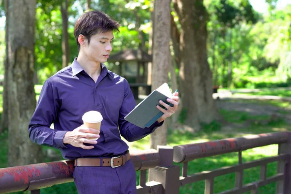 Elinde kahve fincanı olan bir adam ya da bahçede duran yeşil doğa arka planında duran tek kullanımlık kahve ve kitap. Mutlu insanları boş vakitlerinde kabul et ve kahve iç...