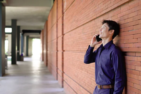 Gülümseyen iş adamı cep telefonuyla dışarıda oturuyor..