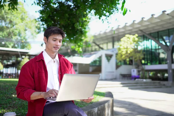 Erkek girişimci açık havada melez olarak oturuyor. Mutlu iş adamı girişimci ofis dışında dizüstü bilgisayar kullanarak başka tarafa bakıyor. Boşluğu kopyala..