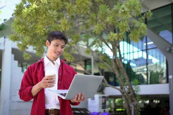 Uzaktan çalışan, kahve içen ve şehir parkında dizüstü bilgisayar kullanan bir adam..